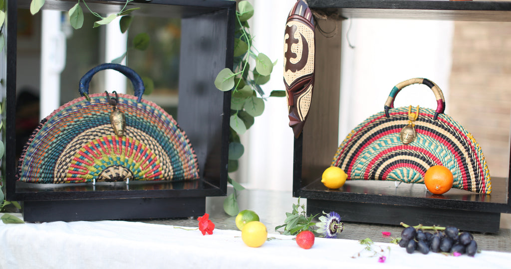 Two colorful handbags on display with fruits and leaves in the foreground.